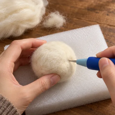 Hands needle felting a wool core on a foam pad